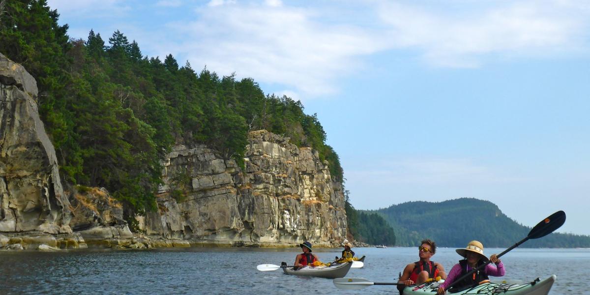 Kayakers paddle past cliffs of Valdes Island
