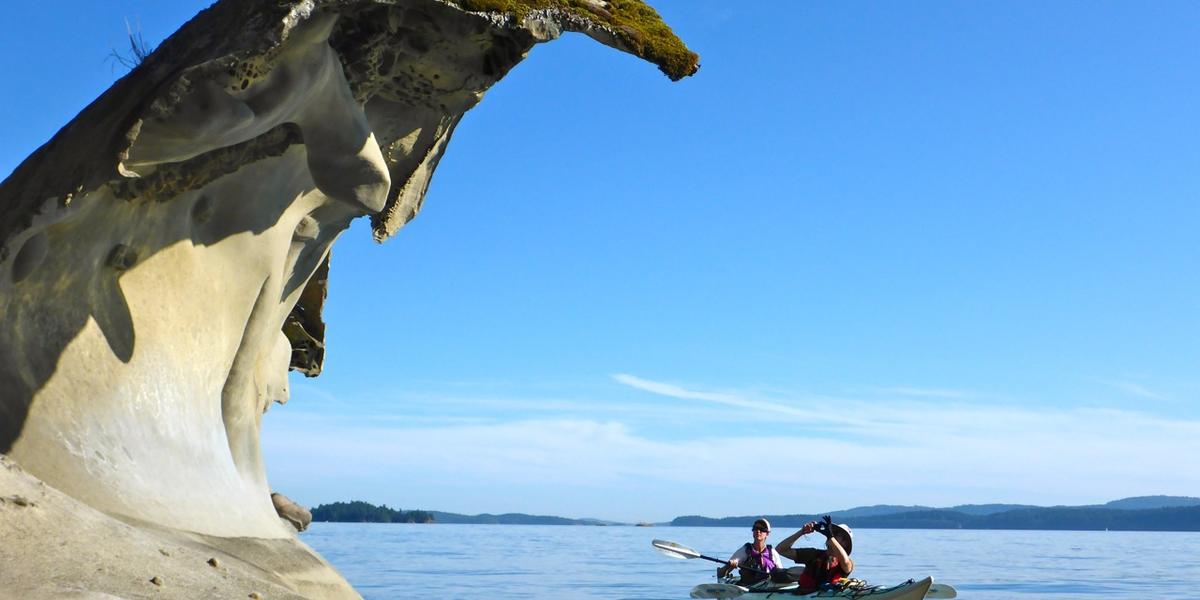 Kayakers paddle under sculpted sandstone overhang